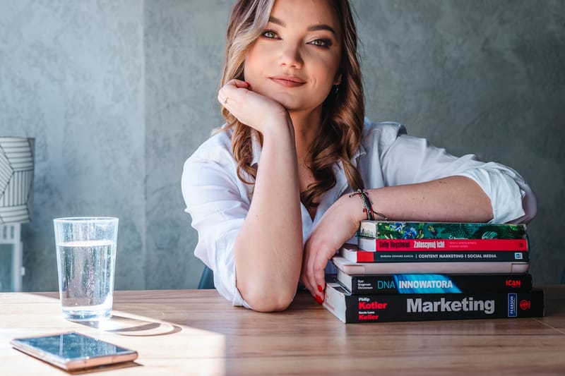 Ewelina Bobak z głową opartą na dłoni przy stosie książek o marketingu