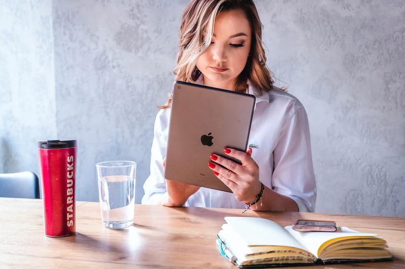 Ewelina Bobak z tabletem przy stole, obok notatnik i kubek